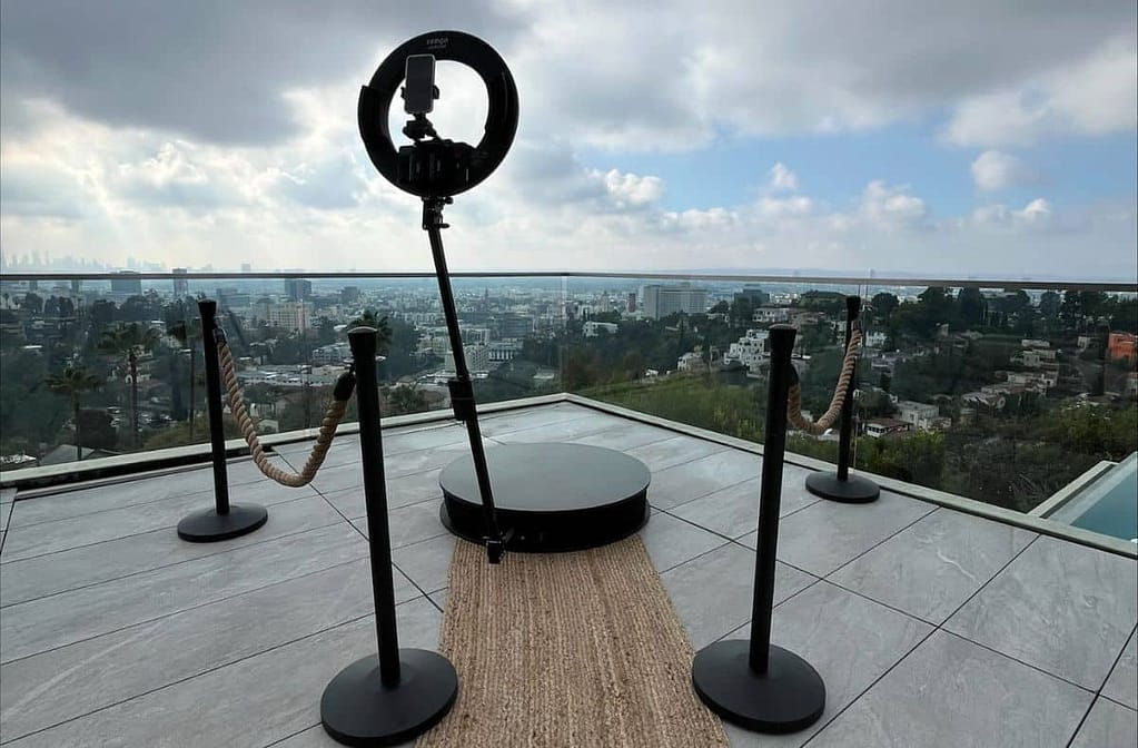 A 360 photo booth setup on a rooftop overlooking a panoramic cityscape under cloudy skies.