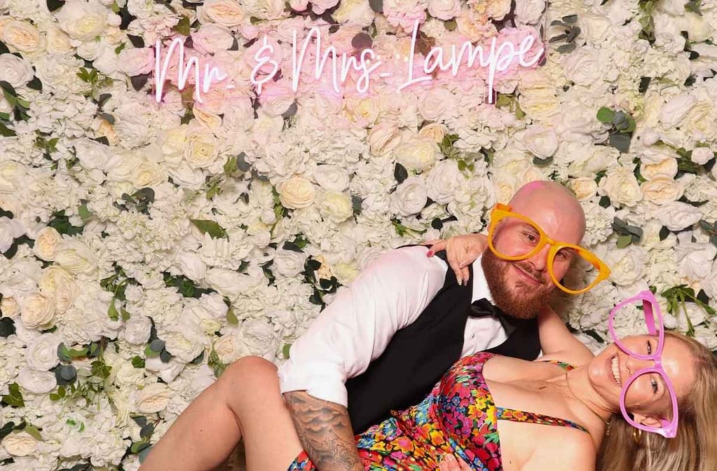 a couple posing for a photo in front of a floral backdrop