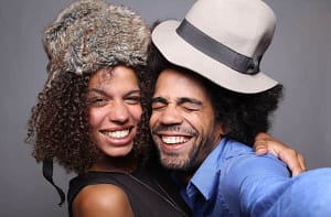 A joyful couple wearing hats, smiling, and taking a close-up selfie in a photo booth.