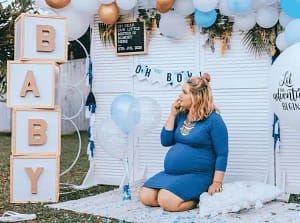 A mom-to-be in blue dress in front of a baby shower backdrop