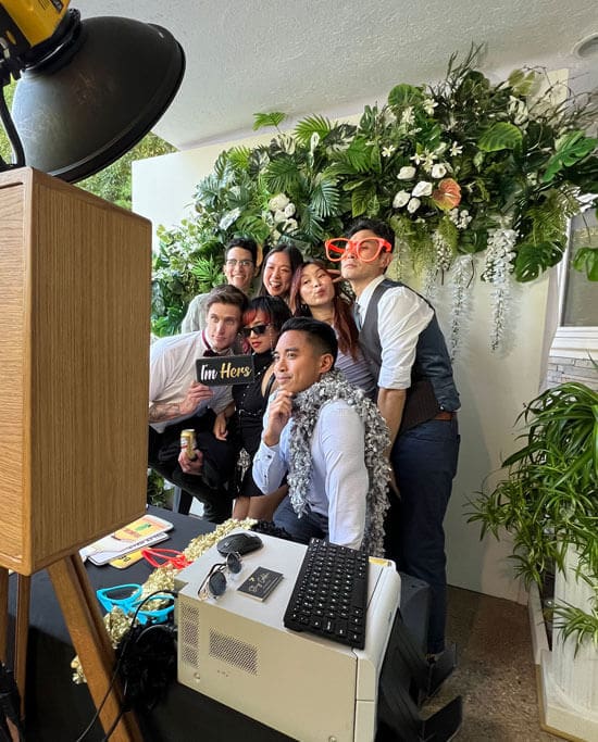 Group posing with props in a photo booth with floral backdrop in San Diego, CA
