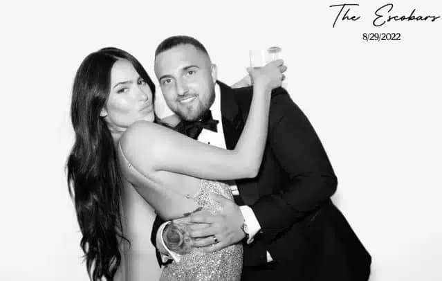 Newlyweds posing in a photo booth at their wedding with a black and white filter, dressed in elegant attire.