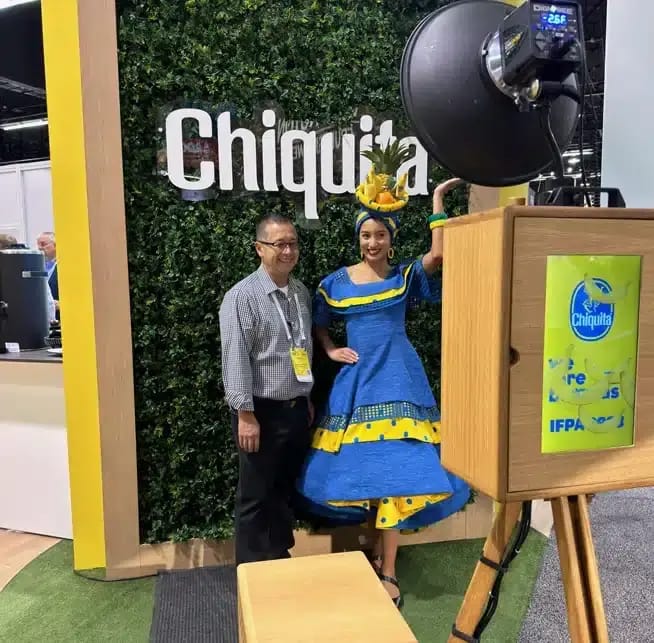 Man poses with a woman in a blue and yellow dress with a fruit hat at Chiquita’s event brand activation photo booth.