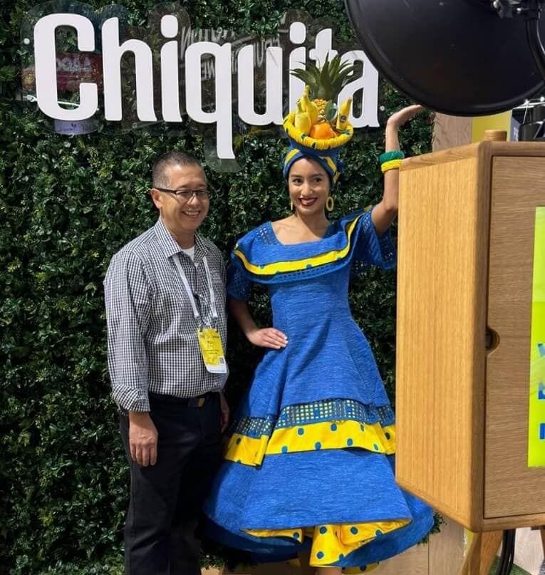 Man poses with a woman in a blue and yellow dress with a fruit hat at Chiquita’s corporate event photo booth.