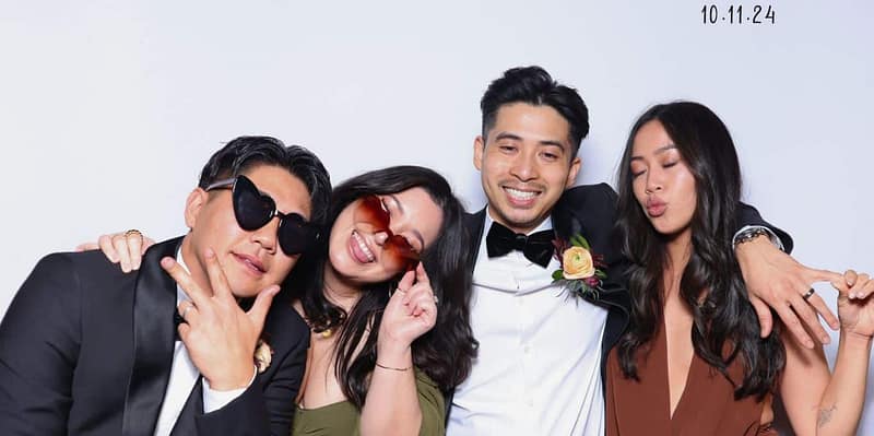 Four wedding guests posing playfully at The Rico Wedding's photo booth rental in Anaheim, smiling and laughing.