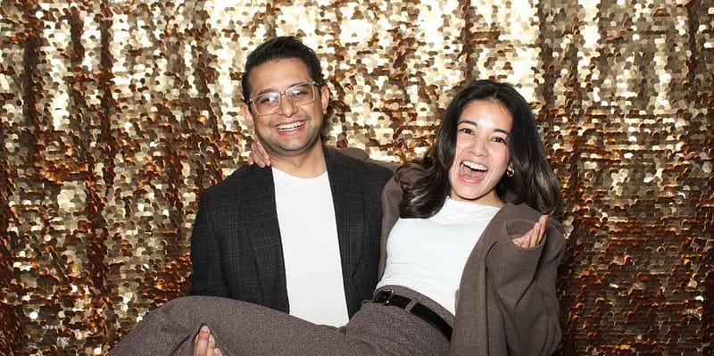 Smiling couple with gold sequin backdrop posing playfully at a photo booth rental in Corona.