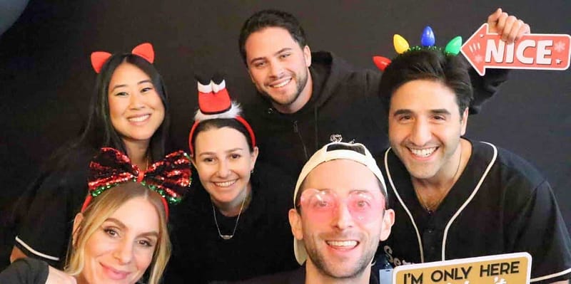 A group of friends posing with festive props at the Service Titan photo booth rental in Laguna Beach, smiling.