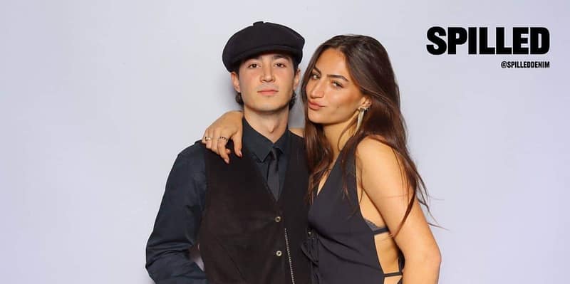 A stylish couple posing at the Spilled Denim photo booth rental in Oceanside, dressed in chic black outfits.