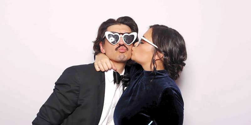 Couple kissing in heart glasses at wedding with photo booth rental in Orange County.