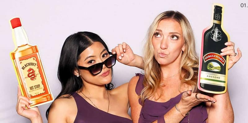 Two women in purple dresses posing with beverage props at a photo booth rental in Torrance.
