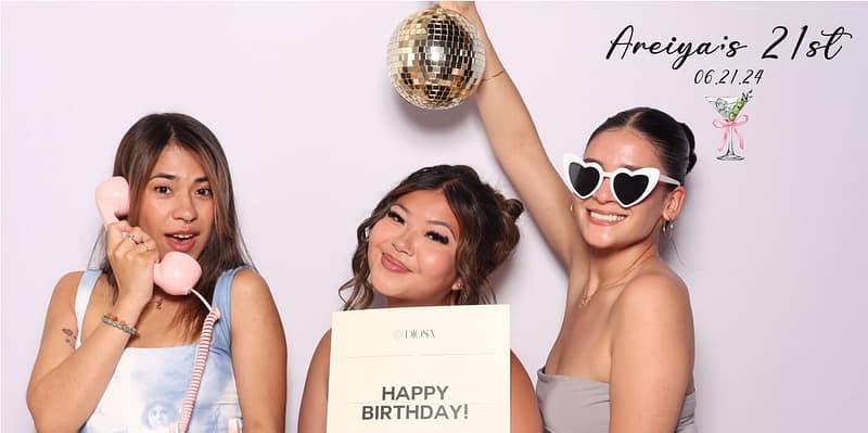 Three ladies posing at Areiya's 21st birthday photo booth in Pasadena, holding props and smiling.