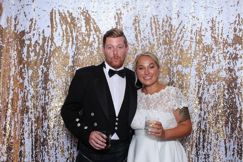 Bride and groom smiling in a gold sequin photo booth.