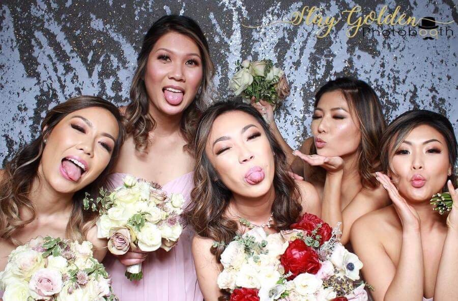 Bridesmaids making playful faces and holding bouquets in a photo booth.