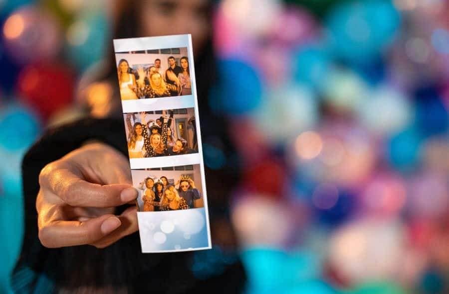 Hand holding a photo booth strip with three group photos in a colorful background