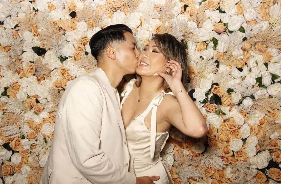 Couple sharing a kiss in front of a floral wall backdrop at Charity and Robert’s wedding photo booth
