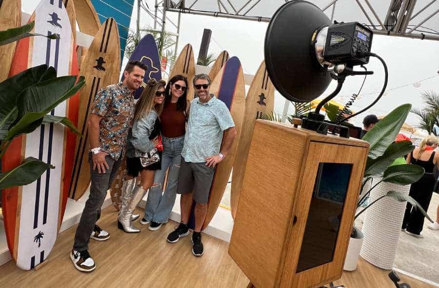 A group poses at a surf-themed with glam photo booth for corporate events, featuring a pro lighting setup.
